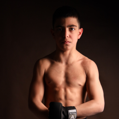 Mark Ghambaryan in MMA shorts and gloves showing athletic physique in dramatic half lighting.